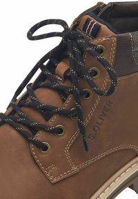 Botte en cuir brun avec des lacets bleu foncé, des œillets dorés et un panneau texturé contrastant. Elle présente une semelle blanche cousue et un logo de marque.