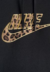 Sudadera negra con un contorno dorado elevado del logo "Nike" con un patrón de estampado de leopardo en el interior, en contraste con el fondo de la tela.