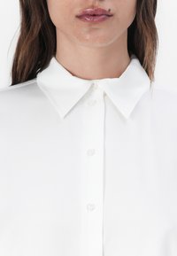 White collared shirt with a smooth texture, featuring a button-down front and a classic collar design.