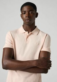 Ljusrosa polo t-shirt med korta ärmar, en klassisk krage och två knappar. Tyget verkar mjukt och slätt med en subtil lyster.