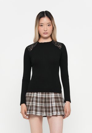 Haut noir à manches longues avec texture côtelée et accents en dentelle aux coutures des épaules, associé à une mini-jupe évasée en tartan dans des tons de marron et de blanc.