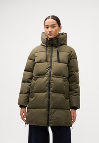 Olivenfärgad puffjacka med hög krage, svart dragkedja och justerbara snoddar. Har en fyrkantig quiltad design och sidofickor.