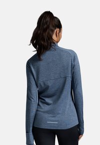 Maglia sportiva a maniche lunghe in tessuto blu testurizzato con colletto alto, dotata di un pannello posteriore senza cuciture e di un accento riflettente sull'orlo.