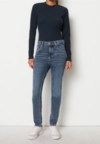 Džínsy s vysokým pasem, modré s vybledlým odstínem, rovného střihu, s pěti kapsami a kovovým knoflíkem, v kombinaci s tmavě modrým žebrovaným topem s dlouhým rukávem.