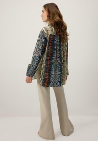 Večbarvna bluza z vzorci kačje kože in geometrijskimi vzorci v modri, oranžni in bež barvi, kombinirana z bež širokimi hlačami.