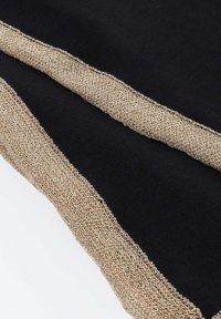 Tissu noir avec large bordure tricotée beige le long des bords, présenté en diagonale sur une surface blanche.