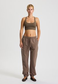 Hnedý atletický krátky top v kombinácii s voľnými hnedými teplákmi. Nohavice majú elastický pás a lem, pričom sú vybavené bočnými vreckami.