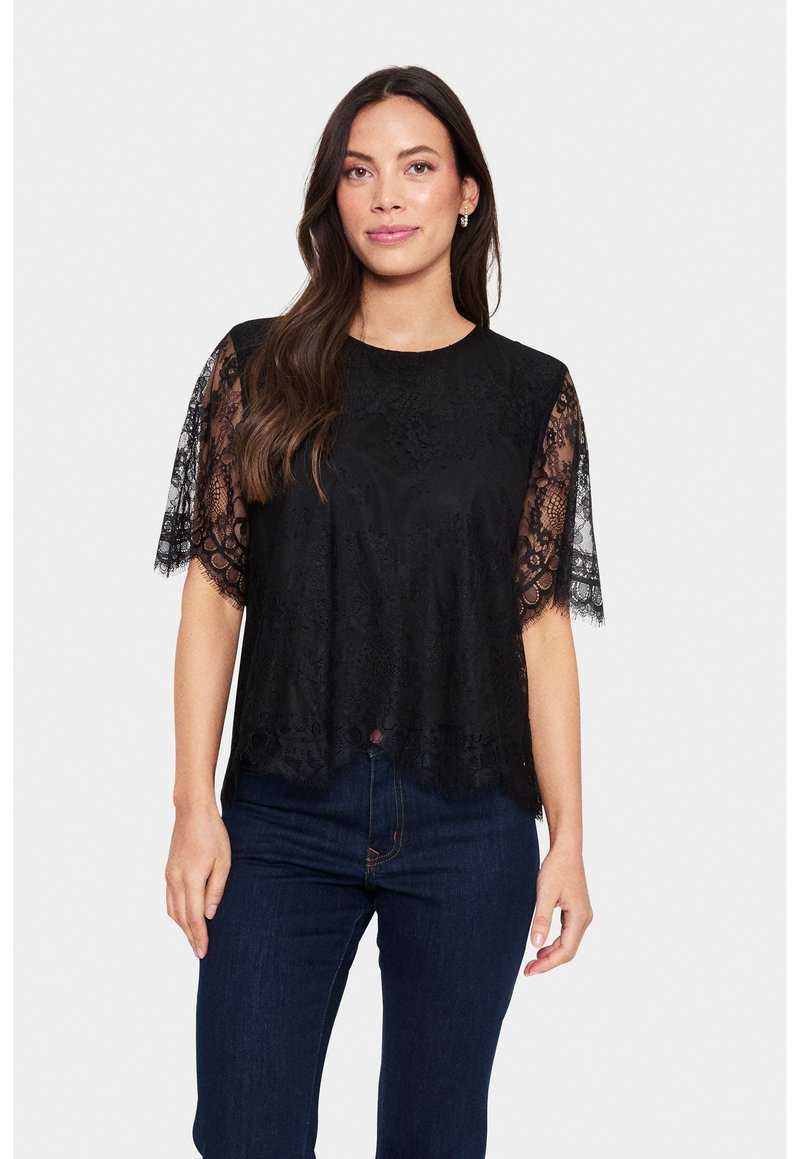 Black lace top with short, sheer lace sleeves, textured fabric, round neckline, and a scalloped hem, paired with dark jeans.