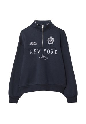 Tamno plava dukserica s visokim ovratnikom, polu-zipom i rebrastim rukavima. Ima bijeli natpis "NEW YORK" i ukrase na prsima.