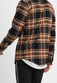 Karierte Flanellshirt in Schwarz-, Braun- und Orangetönen. Mit langen Ärmeln, abgerundetem Saum und lässiger Passform. Aus weichem Stoff gefertigt.