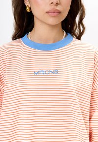 Gestreiftes T-Shirt mit orange- und weißen horizontalen Streifen, einem hellblauen gerippten Kragen und der Aufschrift "MÍRONS" in Blau auf der Vorderseite.