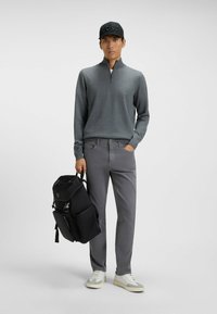 Szary sweter z zamkiem, szare spodnie, białe i szare sneakersy, czarny plecak oraz czapka z tłoczonym logo. Minimalistyczny i nowoczesny design.