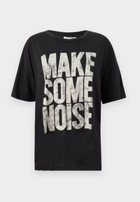 Μαύρο βαμβακερό t-shirt με μεγάλα, φθαρμένα λευκά γράμματα που γράφουν "ΚΑΝΕ ΚΑΤΙ ΘΟΡΥΒΟ." Κοντά μανίκια και χαλαρή εφαρμογή.