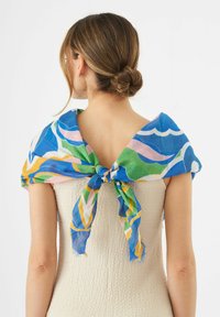 Écharpe légère et multicolore nouée autour des épaules, ornée de motifs ondulés en bleu, vert, rose et jaune. Bords effilochés visibles.