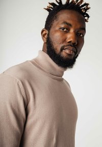 Beige coltrui gemaakt van zachte, gestructureerde stof. Heeft een geribde kraag en manchetten, een slim fit ontwerp en een naadloze zijkant.