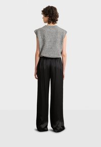 Graues ärmelloses Stricktop kombiniert mit schwarzen weiten Hosen. Sanfte Textur, lockere Passform und Faltendetails an den Hosen.