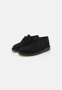 Chaussures en suede noir avec un design simple à lacets, bout rond et semelle en caoutchouc texturé contrastant. Texture lisse avec un minimum de couture.
