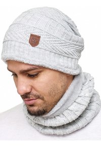 Gray knitted beanie with a plush inner lining and a leather logo patch, paired with a matching textured cowl scarf in a similar gray tone.