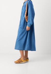 Denimkjole med lange ærmer og to forlommer, parret med brune og gule sneakers med tre striber og en struktureret design.