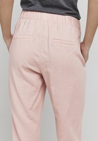 Lys rosa, løstsittende bukser med elastisk midje, to baklommer og en teksturert stofffinish.