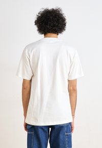 T-shirt branco de algodão com um corte descontraído, mangas curtas e decote redondo, mostrado pela parte de trás; combinado com calças de ganga azuis.