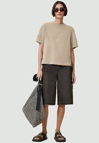 T-shirt de algodão bege com letras em relevo, combinada com calções de ganga escura. Saco tote em padrão preto e branco e sandálias castanhas.