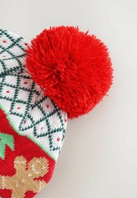 Knitted Christmas hat with red pom-pom, white and green diamond pattern, and gingerbread man design on red background.