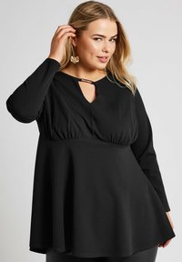 Mustapaita pitkähihaisilla hihoilla ja avonaisella kaula-aukolla. Laskostettu muotoilu ja kerätty vyötärö tarjoavat rakennetta. Valmistettu pehmeästä, joustavasta kankaasta.