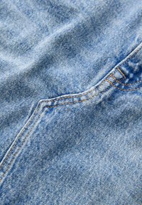 Lyseblåt denimstof med en let falmet tekstur, der har synlige orange syninger. Det viser en glat, blød overflade med en tydelig struktur.