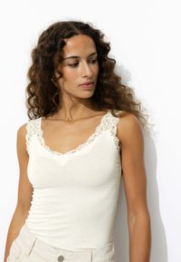 Débardeur beige avec un col en V, ornée de délicates accents en dentelle sur les bretelles. Tissu doux avec une coupe ajustée pour un look élégant.