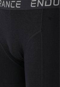 Svarta boxershorts med en bred elastisk midja som har texten "ENDURANCE" i grått. Tillverkade av ett slätt tyg med synliga stygn.