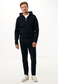 Černá mikina s kapucí a předním zipem, doplněná o černé kalhoty a bílé tenisky. Hladký materiál, volný střih.