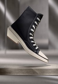 High-top shoes featuring a black fabric upper, white rubber sole, and laces, with contrasting stitching and a rounded toe design.