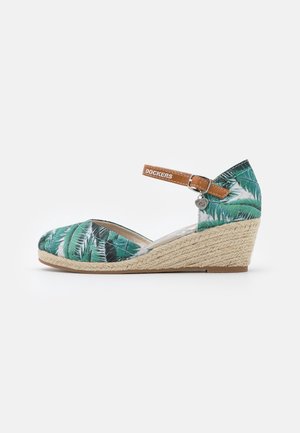 Wedgesandaal met een patroon van groene palmbladeren, een tankleurige enkelband met het label "Dockers" en een gevlochten jutezool.