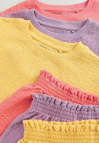Vier T-Shirts in Pastellfarben gestapelt: gelb, rosa, lavendel und pfirsich. Sie verfügen über einen strukturierten Stoff mit gerippten und gerafften Details.