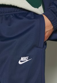 Námořnické sportovní kalhoty vyrobené z hladké látky, s bílým logem Nike na boku, s jemnými elastickými detaily a kapsami.