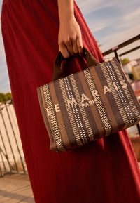 Sac à main rayé marron avec un motif texturé, souligné par l'inscription blanche « LE MARAIS PARIS ». Doté de poignées courtes marron, forme rectangulaire.