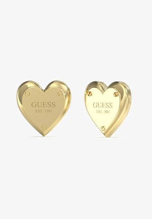 Orecchini a forma di cuore in oro con incisione "GUESS EST. 1981." Ogni orecchino presenta una superficie liscia e riflettente e quattro fori di montaggio.