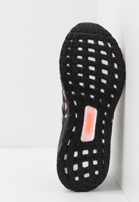 Suela de zapatilla de goma negra con banda de rodadura multidireccional, que presenta una unidad de amortiguación pronunciada en color naranja translúcido y acentos multicolores.