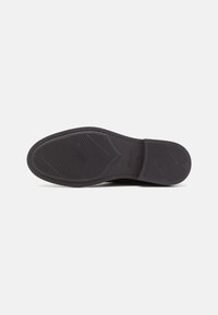 Black rubber shoe sole with textured grip pattern, featuring a slight curve at the heel and reinforcing grooves for traction.