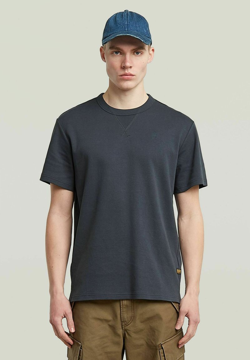 Donkergrijze T-shirt met een ronde hals, korte mouwen en een subtiele logo. Draag het met lichtbruine cargoshorts. Een lichte denim pet maakt de look compleet.