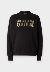 Felpa nera in cotone con colletto rotondo e maniche lunghe. "VERSACE JEANS COUTURE" è in evidenza in caratteri metallici dorati.
