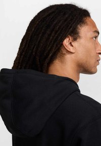 Hoodie nero con vestibilità comoda, grande cappuccio posteriore e dettagli di cucitura visibili, mostrato da una vista laterale.