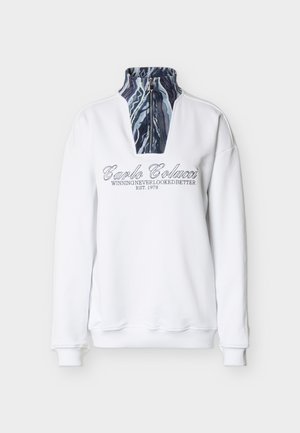 Sweat-shirt blanc à col montant, avec une fermeture éclair partielle et une doublure intérieure à motif. Texte graphique gris à l'avant.
