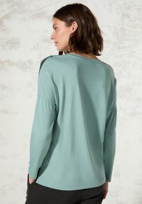 Jasnoniebieska koszula z długim rękawem o luźnym kroju, z plisowanymi rękawami i czarnym akcentem na ramieniu. Miękka, gładka tekstura.