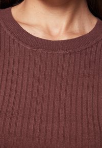 Sweter z prążkowanego materiału w głębokim odcieniu burgundu. Posiada okrągły dekolt i gładką strukturę, eksponując delikatne pionowe linie.