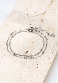 Pulsera de cadena de plata con dos hilos, que presenta cuentas redondas y un cierre de langosta, descansando sobre una superficie de piedra clara y texturizada.