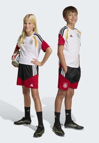 Children's soccer jerseys feature a white base with red accents and black shorts. The design includes stripes and the German football emblem.
