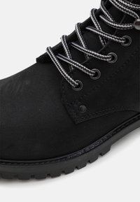 Stivaletto nero con materiale scamosciato liscio, punta rotonda, suola in gomma resistente e lacci grigi e bianchi a fantasia.