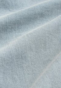 Hellblauer Denimstoff mit feiner, strukturierter Webart, der subtile Farbnuancen und Faltenlinien aufweist. Weiches und geschmeidiges Material.